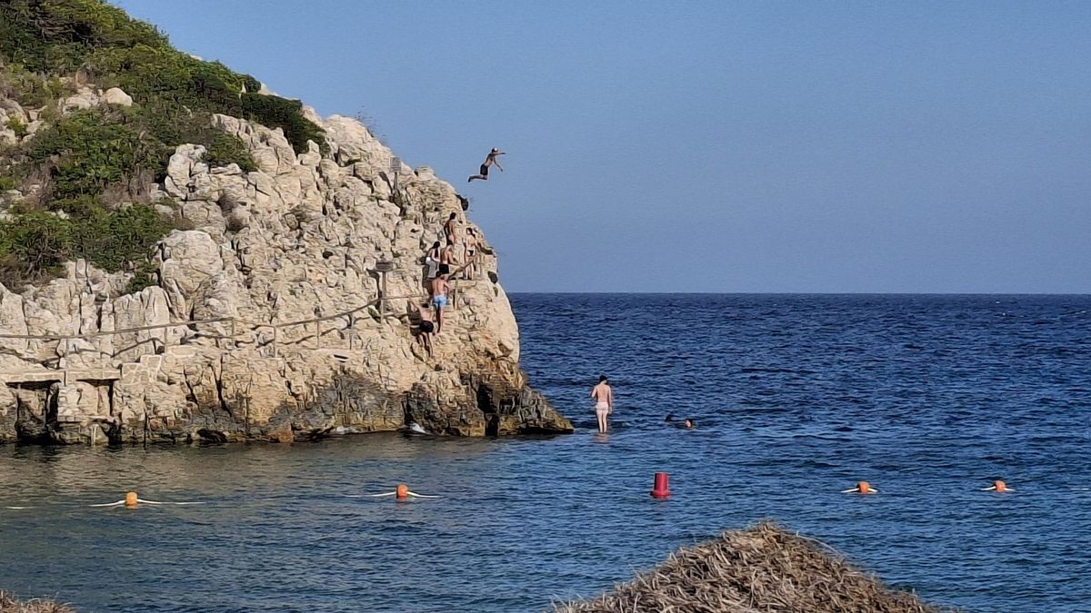 Un bañista salta al mar desde las rocas del extremo norte de la cala de la Granadella