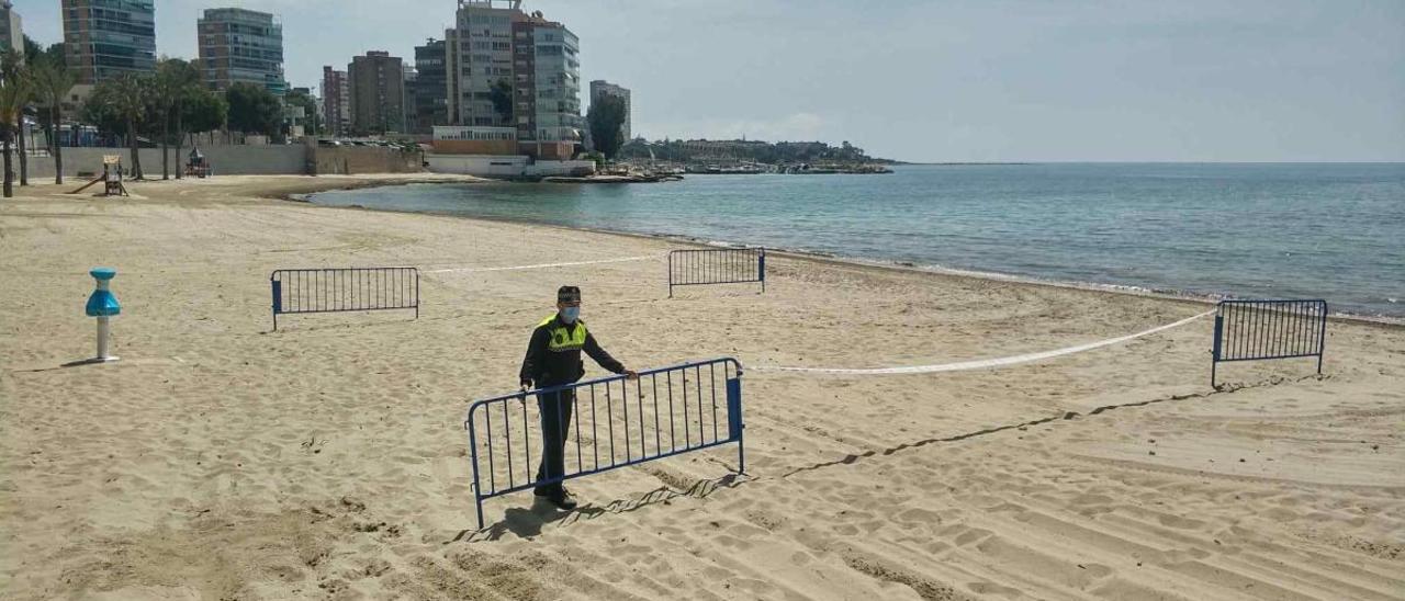 Un policía local coloca vallas para acotar las zonas reservadas a la práctica deportiva profesional en la Albufereta.