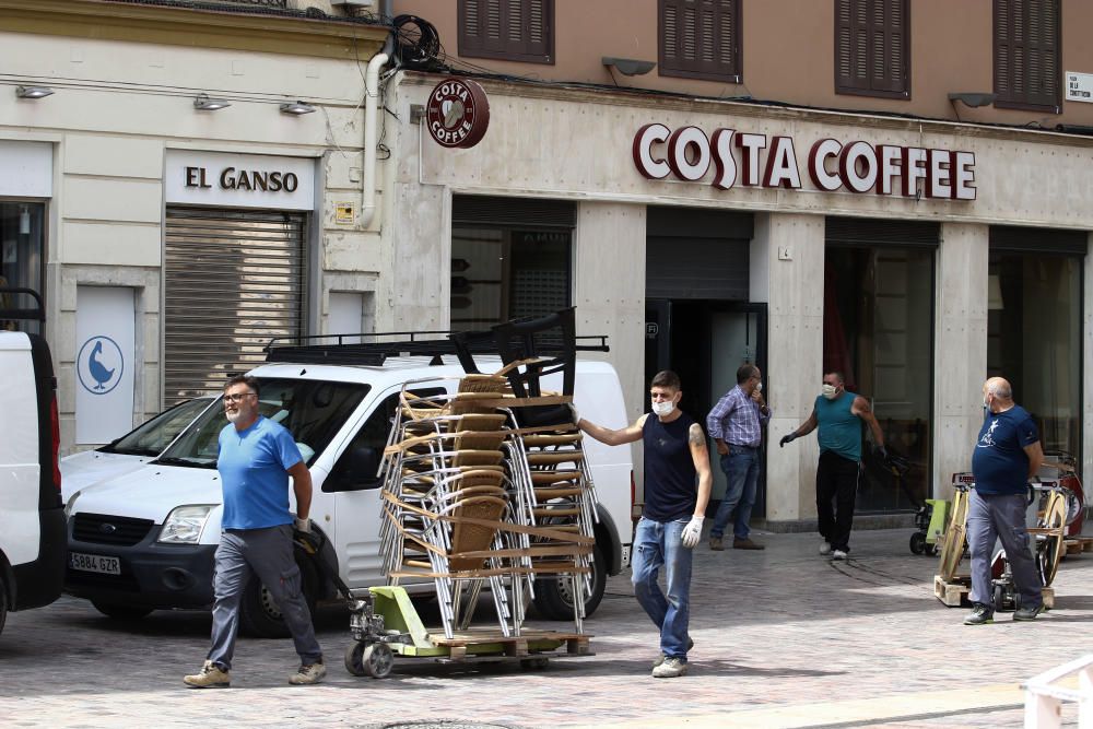 Imágenes de una lluviosa mañana de jueves en el centro de Málaga, donde al paisaje ya habitual de pocas personas y la mayoría de ellas con guantes y mascarillas se le han añadido los preparativos de bares, cafeterías y terrazas que se preparan para el inminente cambio de fase de la desescalada de la ciudad.