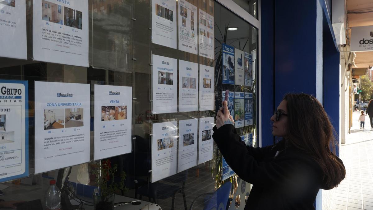 Un joven fotografía un anuncio en una inmobiliaria de València.