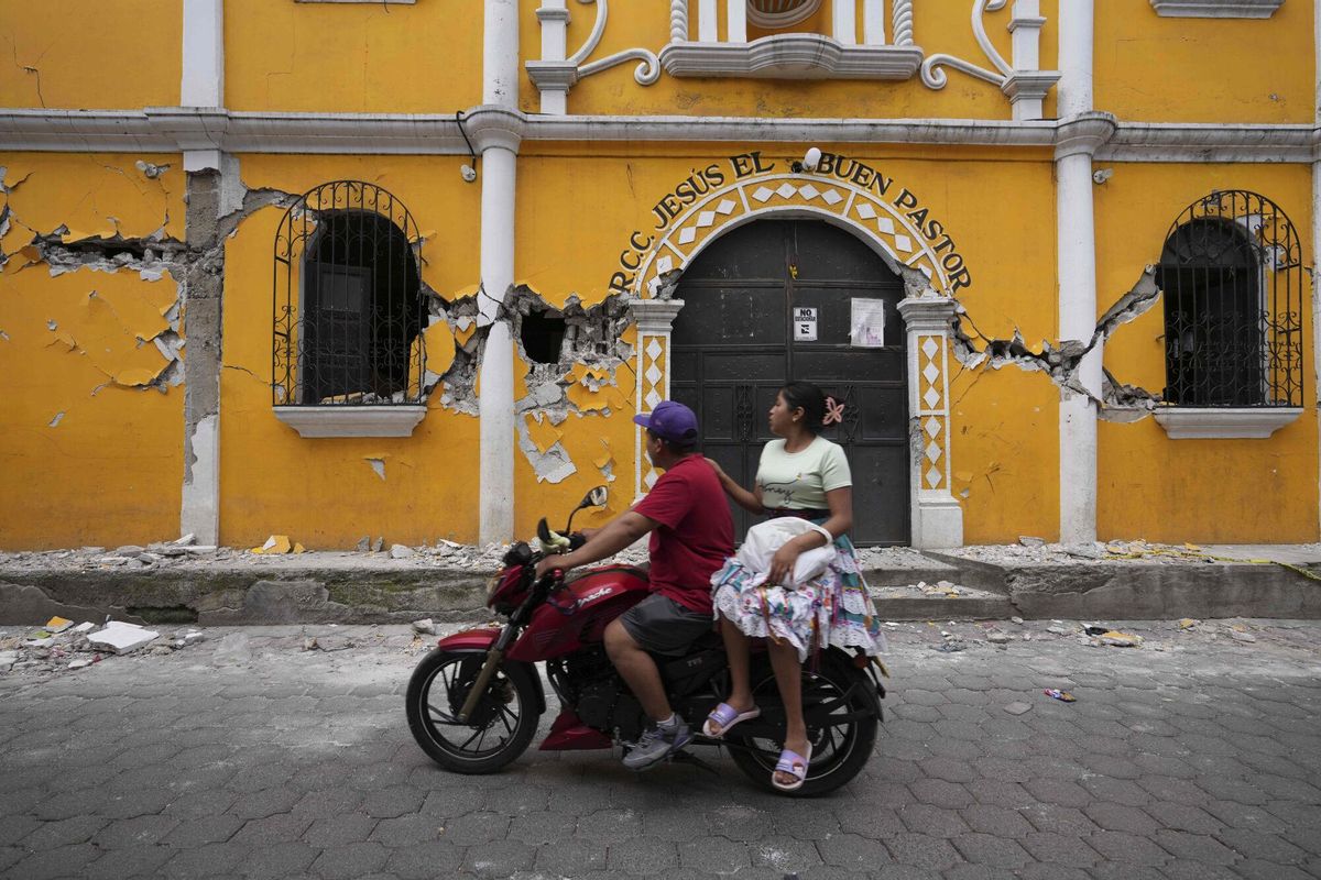 A couple ride past a community hall damaged as a result of dozens of earthquakes and aftershocks recorded in a matter of hours, in Santa Maria de Jesus, Guatemala, Wednesday, July 9, 2025. (AP Photo/Moises Castillo). EDITORIAL USE ONLY/ONLY ITALY AND SPAIN
