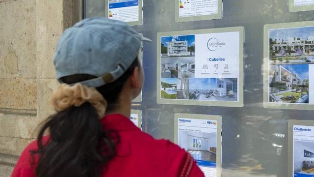Una dona mira anuncis d’habitatges en venda a l’aparador d’una immobiliària de Barcelona.