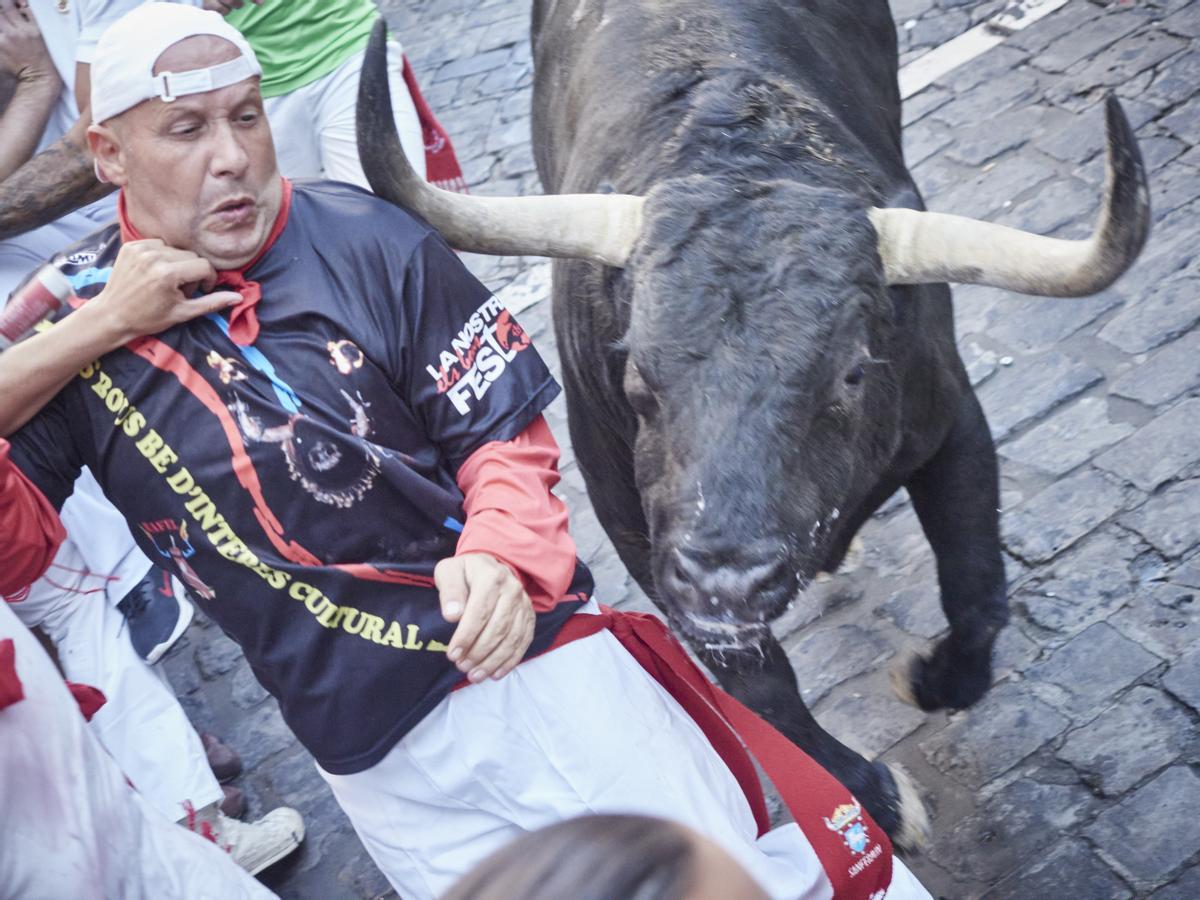 Un toro roza con los cuernos a un corredor durante el segundo encierro de las Fiestas de San Fermín 2022 de la ganadería de Fuente Ymbro.