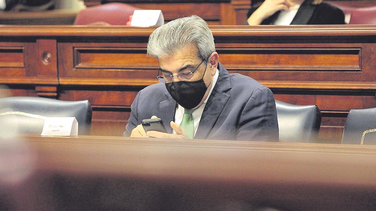 Román Rodríguez, consejero de Hacienda, mira su teléfono móvil durante un pleno del Parlamento de Canarias.