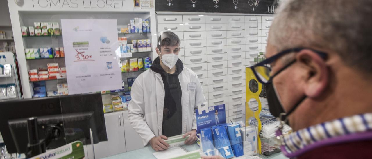 Un farmacéutico atiende a un cliente en una farmacia de Alicante