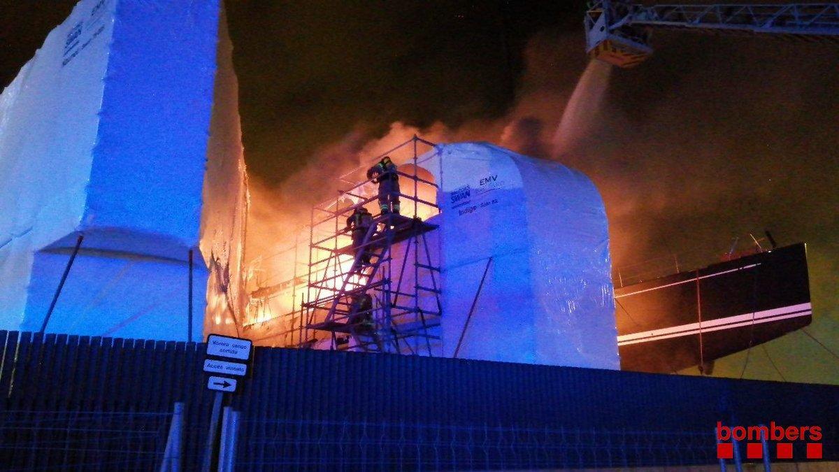 Los bomberos trabajan en la extinción del incendio de un barco en el puerto de Badalona.