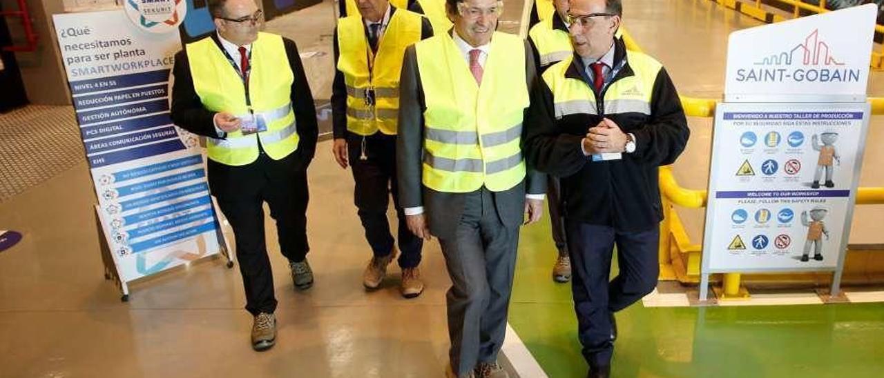 El presidente del Principado, Javier Fernández, en el centro, durante una reciente visita a la factoría de Saint-Gobain y rodeado de carteles donde se informa de los cambios que impulsa la compañía.