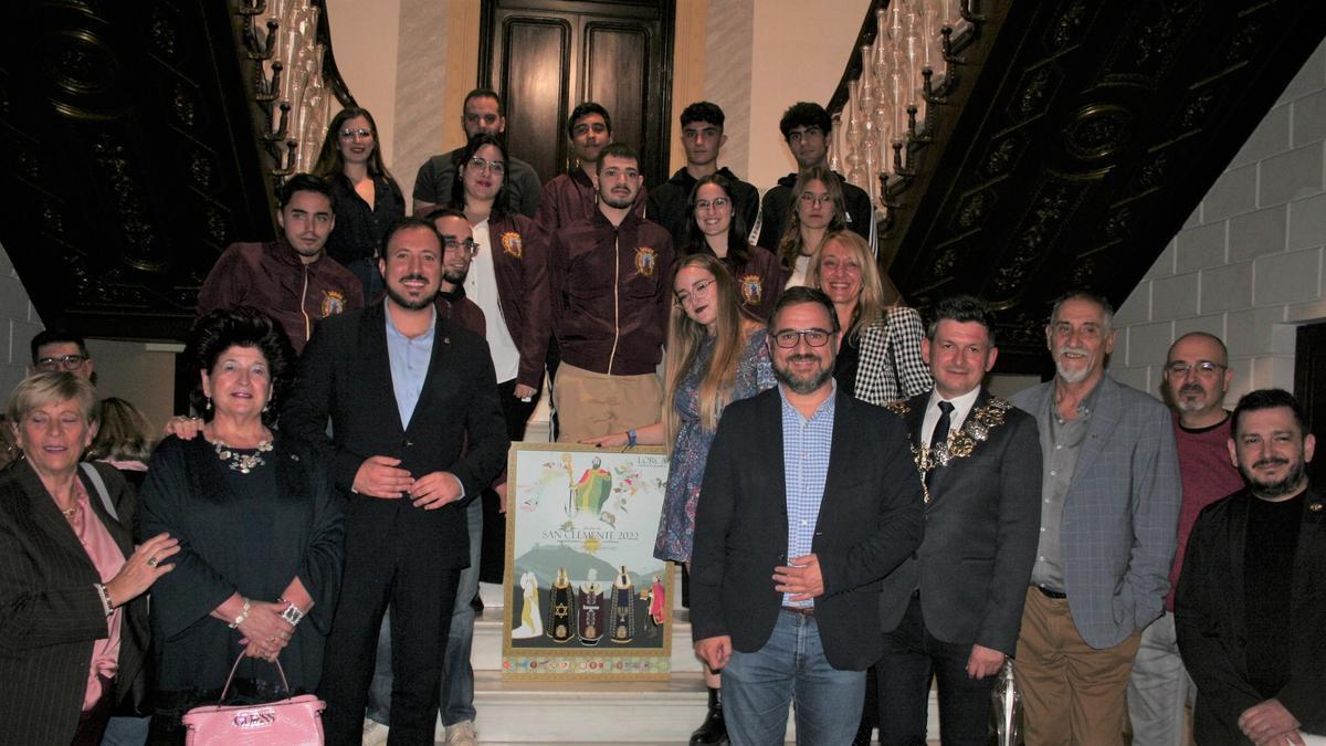 Soledad del Alcázar, Francisco Morales, Natalia Martínez, Diego José Mateos, María Ángeles Mazuecos y Luis Torres del Alcázar con representantes de la sección juvenil de la Federación San Clemente, en las escaleras del Palacete de Huerto Ruano con el cartel de las fiestas patronales.