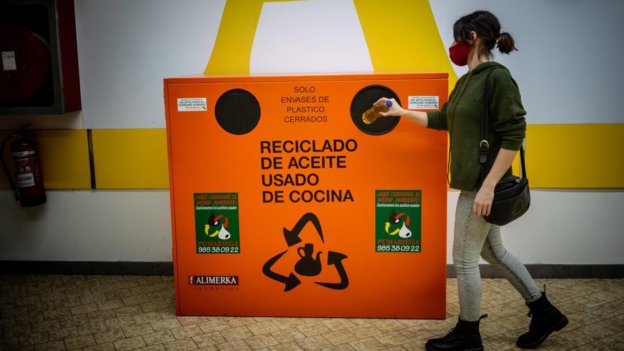 Una usuaria deposita una botella de aceite usado en un contenedor de reciclaje de Pumariega