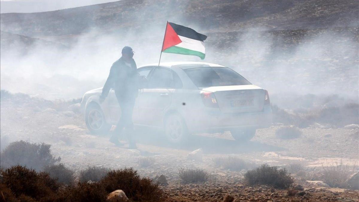 Un hombre ondea la bandera palestina entre gas lacrimogeno en el pueblo cisjordano de Shiyoukh.