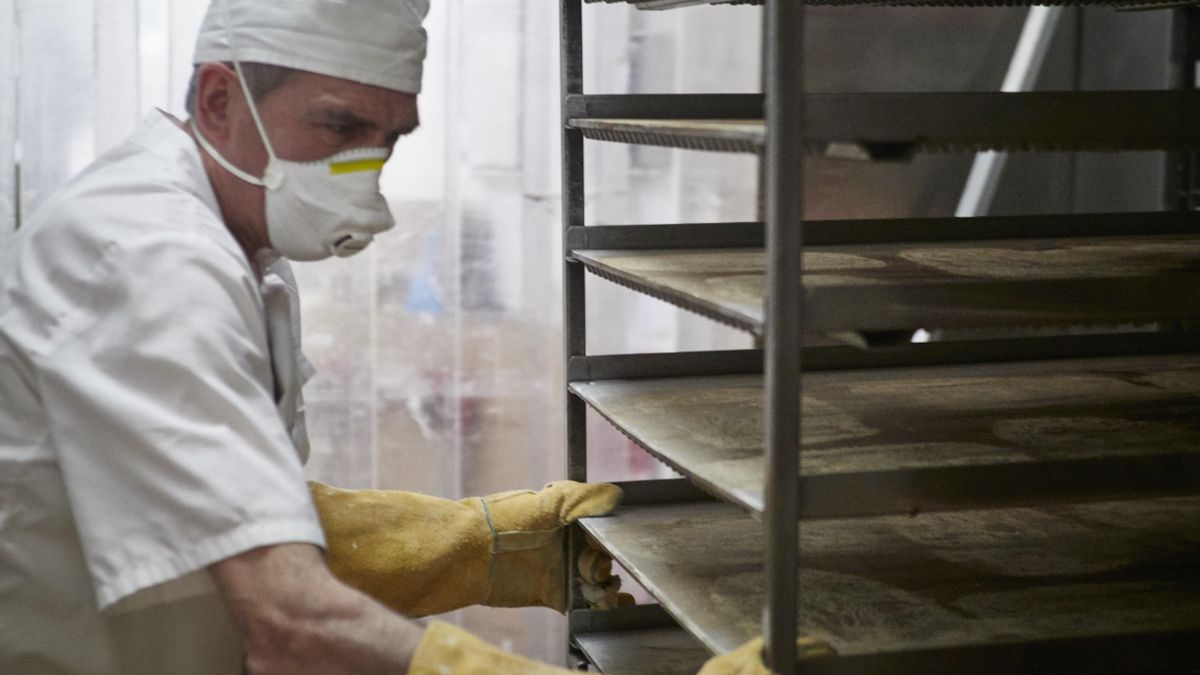 Un trabajador protegido con mascarilla maneja bandejas para cocer pan en una imagen de archivo.