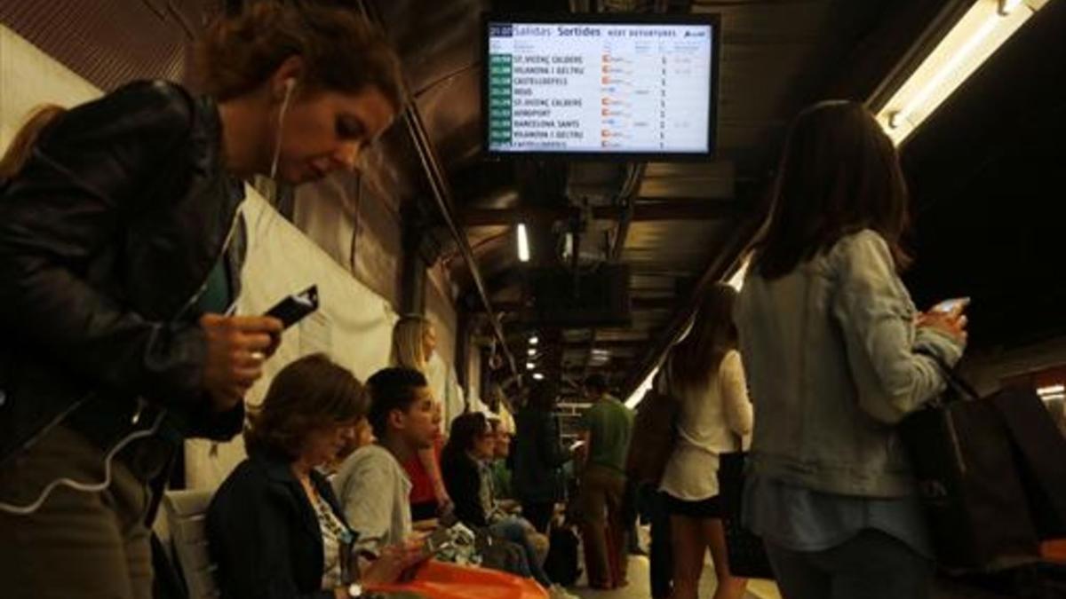 Usuarios de Rodalies esperan en la estación de Passeig de Gràcia, ante un panel que informa de retrasos.