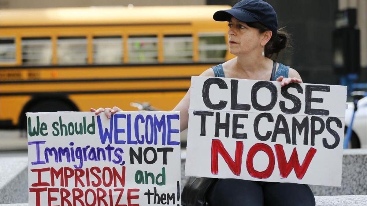Una manifestante sostiene dos pancartas dando la bienvenida a los inmigrantes irregulares y reclamando el cierre de los centros de detención.