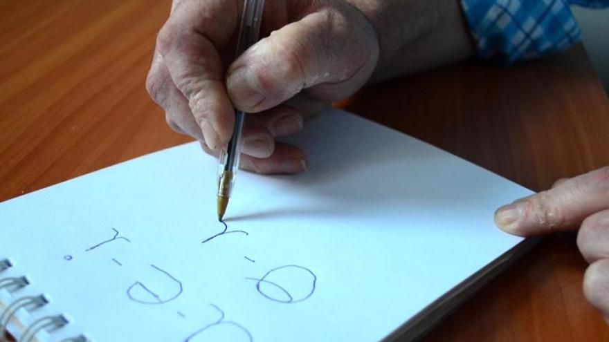 Un hombre escribe las vocales en un cuaderno.