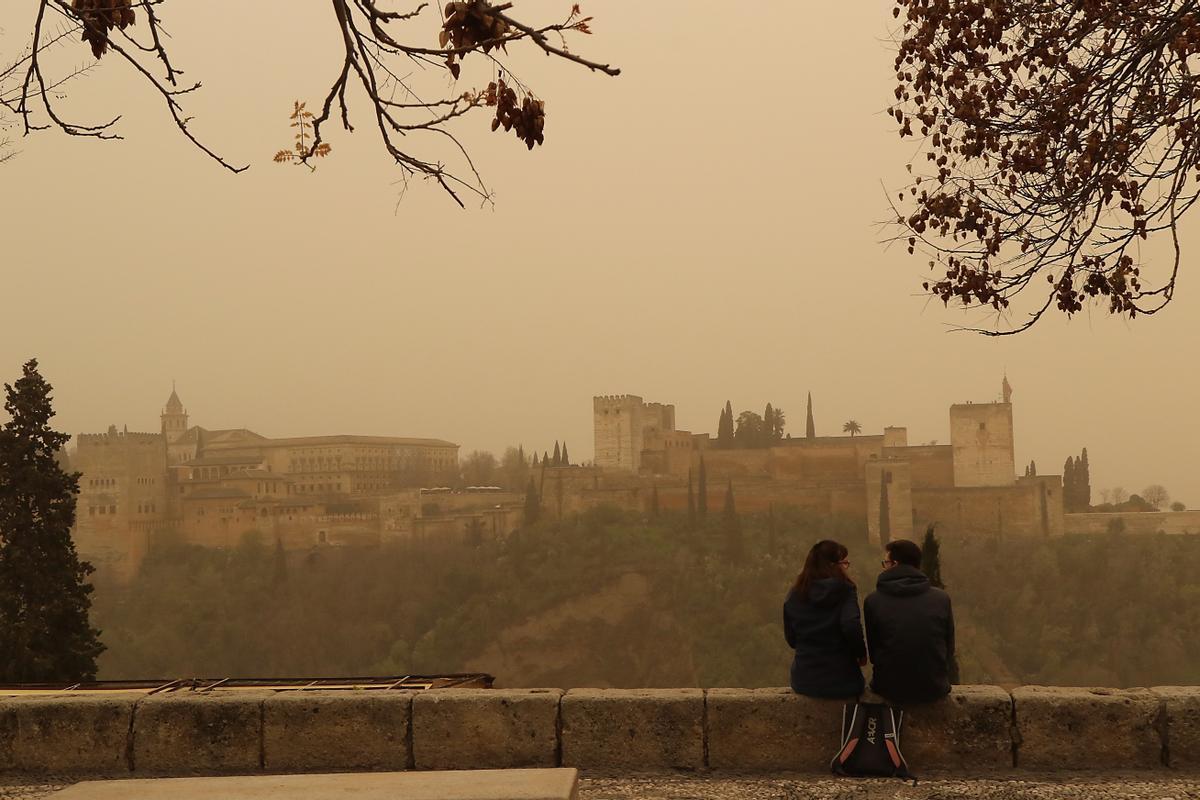 Dos personas observan la Alhambra de Granada desde el Mirador de San Nicolás, con el cielo cubierto por la intensa calima.