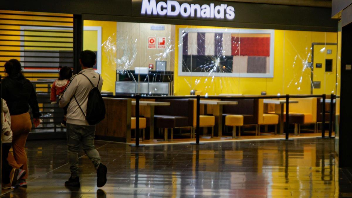 Dos personas pasan delante del escaparate del McDonald's con los cristales rotos en el centro comercial Màgic Badalona, el 27 de marzo de 2024.