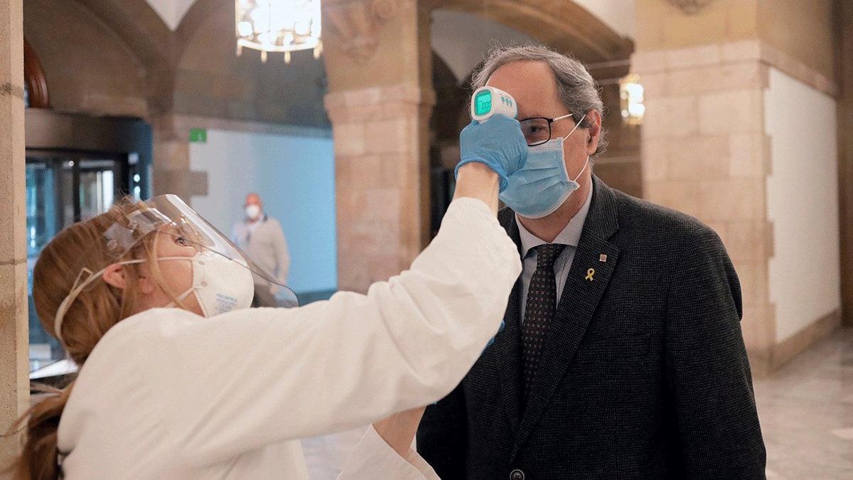 Un miembro de los servicios médicos del Parlament toma la temperatura al presidente de la Generalitat, Quim Torra, a su llegada, el 24 de abril