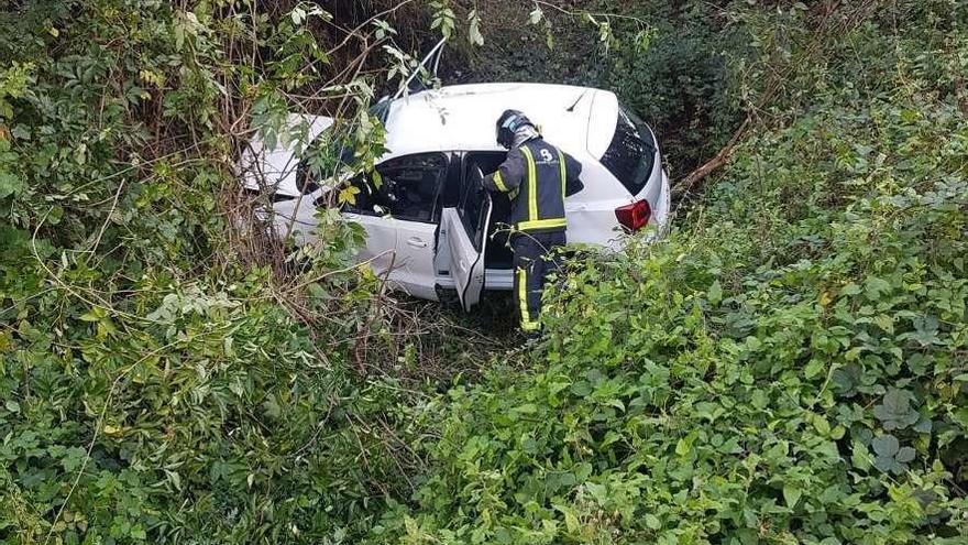 Uno de los bomberos, junto al coche en el fondo del barranco por el que se precipitó.