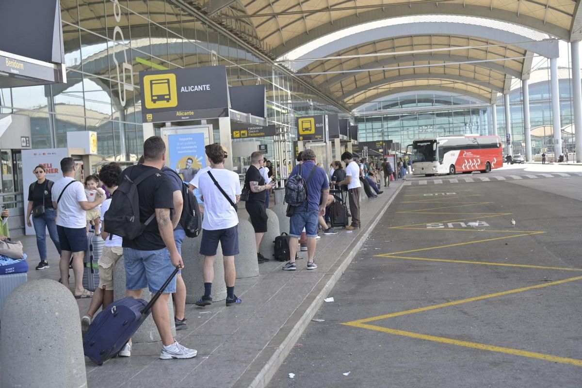 Algunos pasajeros esperando al autobús de Alicante en las puertas del aeropuerto de El Altet en Elche