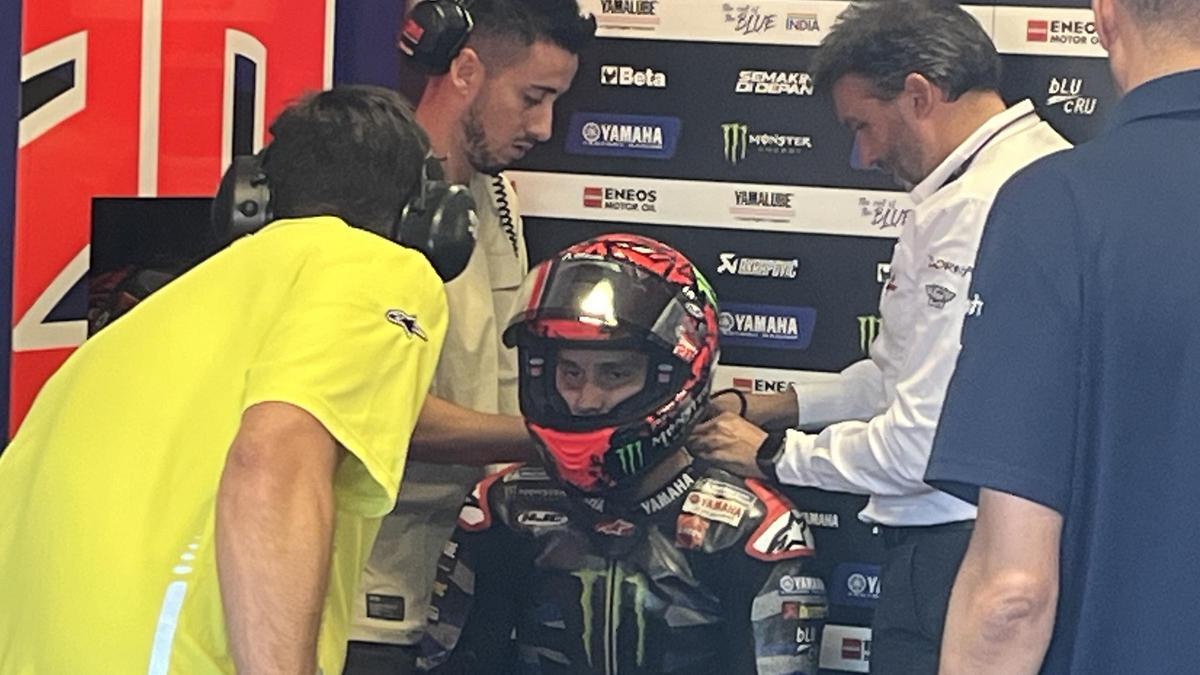 Sergi Sendrá, 'mago' de Dorna TV, con camiseta blanca, ayuda, hoy, a Fabio Quartararo a colocarse el casco especial con radio.