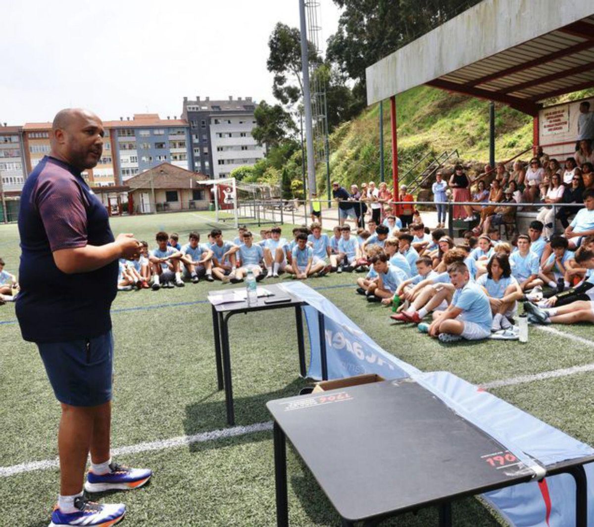 Familias, jugadores, entrenadores y representantes del Ayuntamiento posan frente a la grada principal del campo de fútbol de Raíces con banderas del Real Club Celta de Vigo.