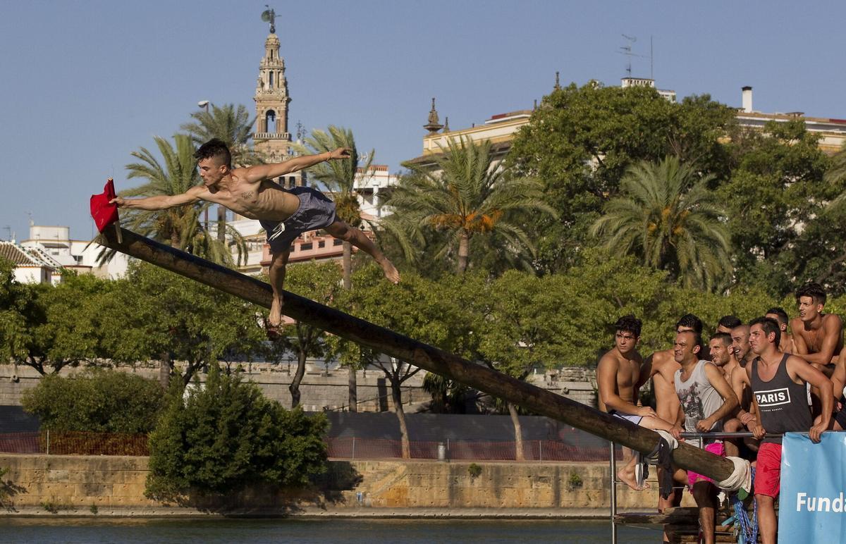 GRA317.- SEVILLA, 23/07/2015.- . Un joven alcanza la bandera de la Cucaña, en el río Guadalquivir, una de las actividades que se celebran con motivo de la "Velá Santa Ana", en el barrio sevillano de Triana. EFE/Jose Manuel Vidal