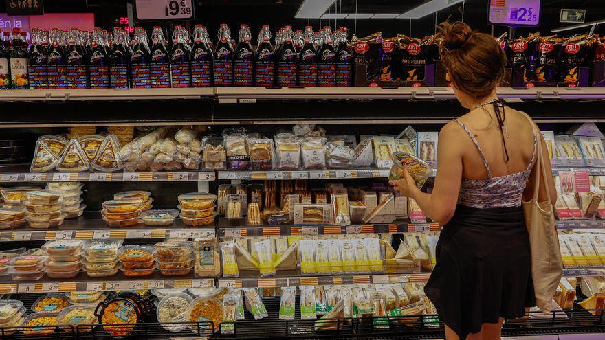 Una mujer contempla la estantería de un supermercado, repleta de productos envueltos en plástico.