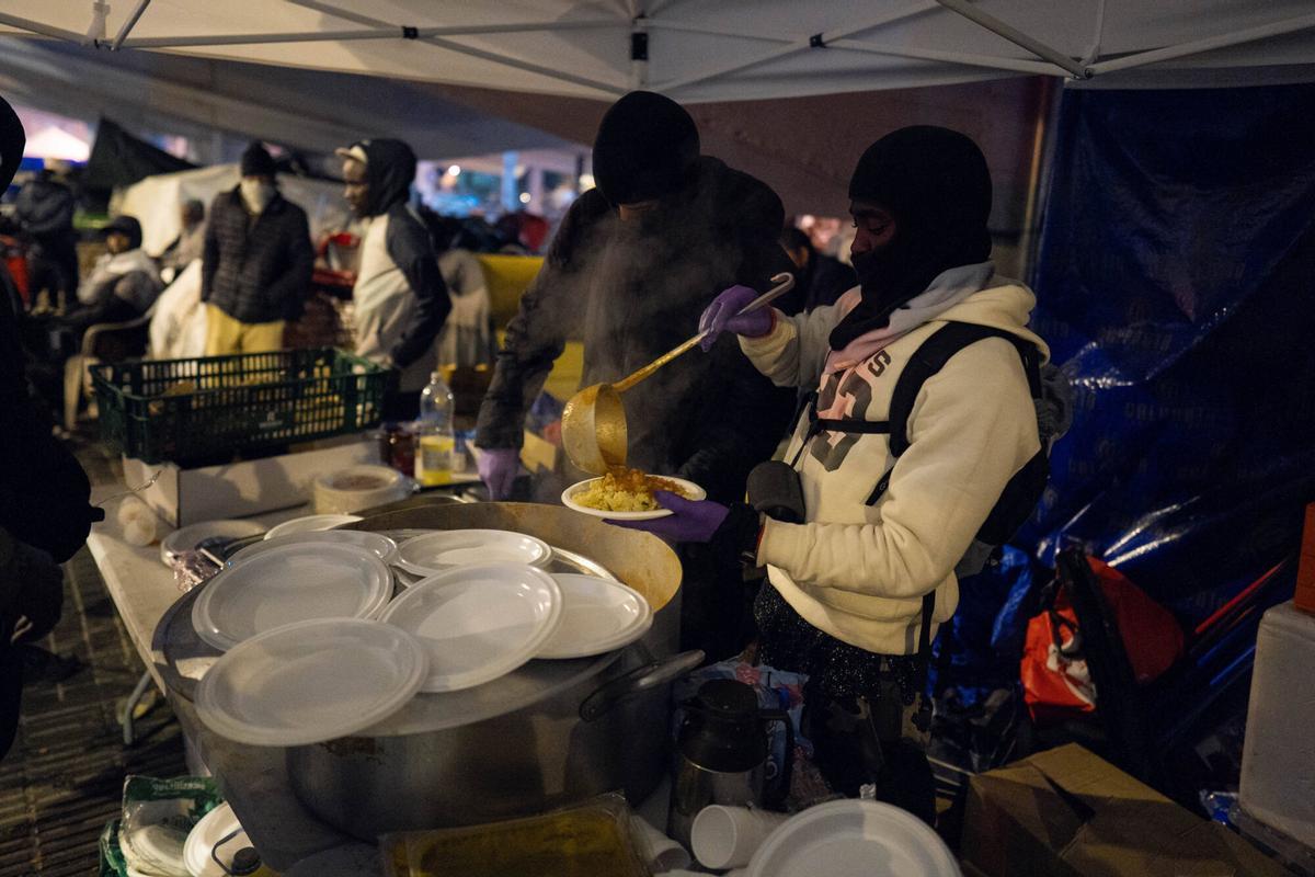 Voluntarios de distintas entidades privadas reparten comida para la cena de Nochebuena bajo la autopista C-31, donde aún duermen decenas de personas desalojadas del antiguo instituto B9