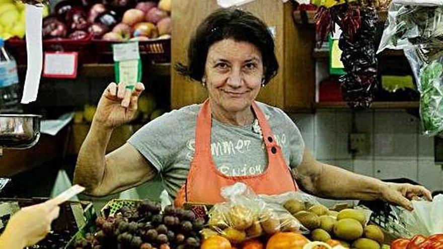 Una frutera atiende a una señora mientras mira sonriente a la cámara.