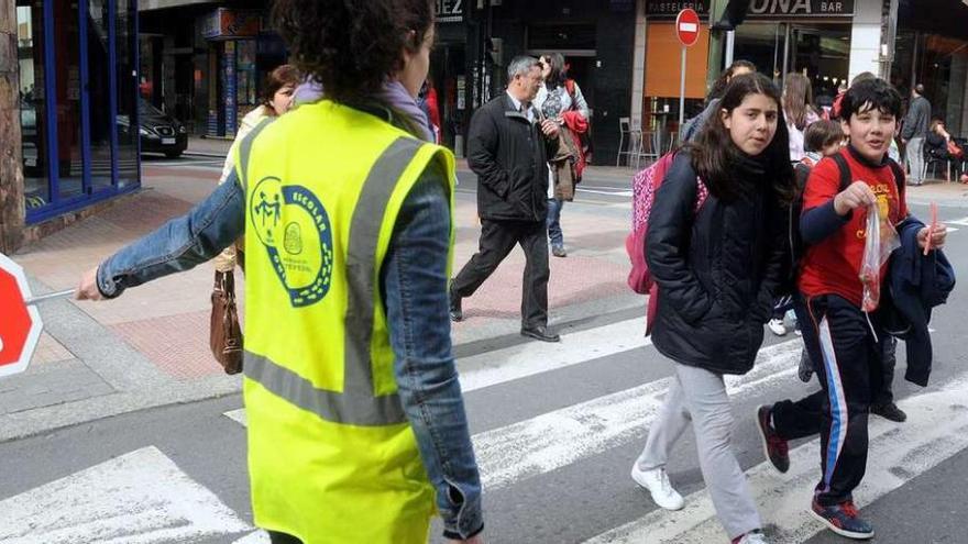 Una de las colaboradoras de los &quot;Camiños Escolares&quot; ayuda a cruzar la calle a unos niños.