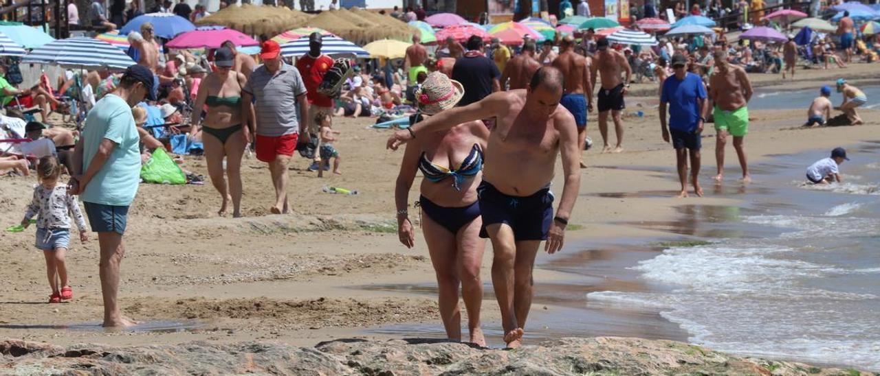 Dos bañistas sortean las rocas que han quedado al descubierto en una playa de Torrevieja