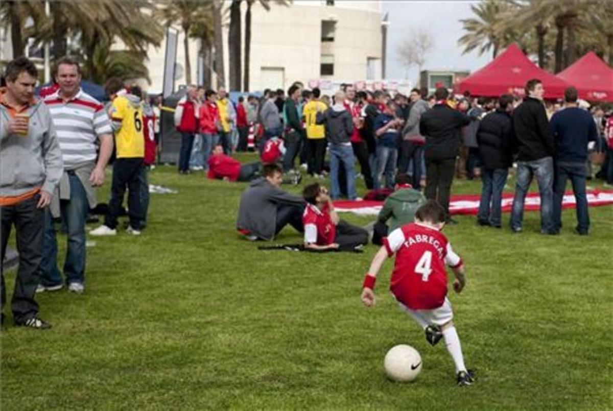 Un nen amb la samarreta de Cesc Fàbregas juga amb la pilota al costat dels seguidors de l’Arsenal, que descansen abans del partit al Camp Nou.