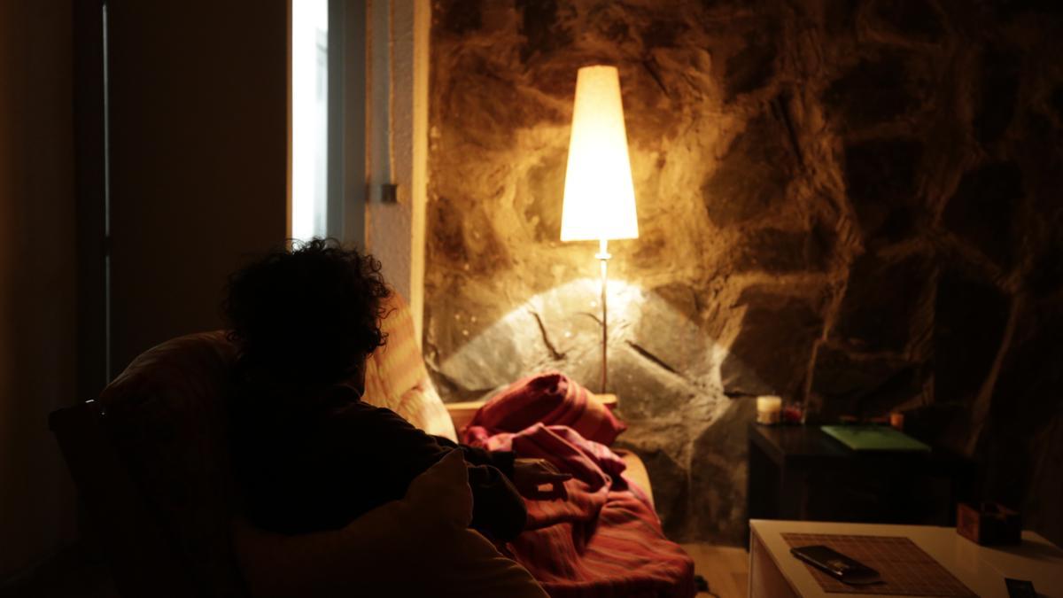 Una mujer descansa en el salón de su casa, a la luz de una lámpara.