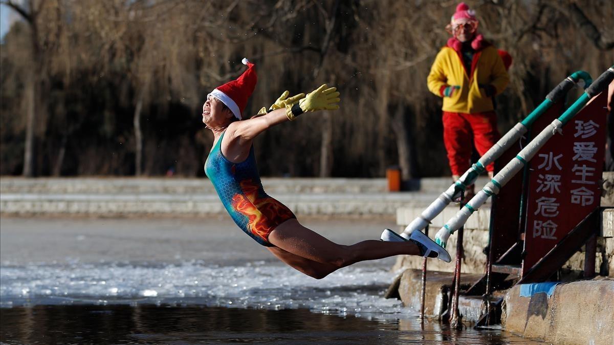 Una mujer con un sombrero de Papá Noel se zambulle en un lago parcialmente congelado en Shenyang, en la provincia de Liaoning, noreste de China. 