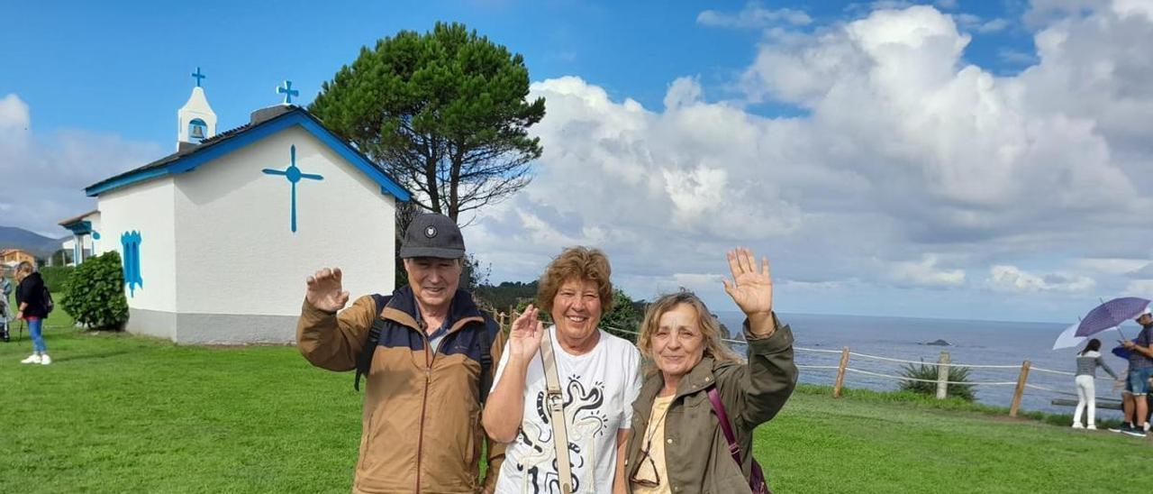 Los madrileños Justo Abril, Benita Rubio y  Leonor Monje, en el  campo de La Garita, en Cadavedo, donde se celebra la popular romería de La Regalina, con el Cantábrico y la ermita a su espalda. | Tania Cascudo