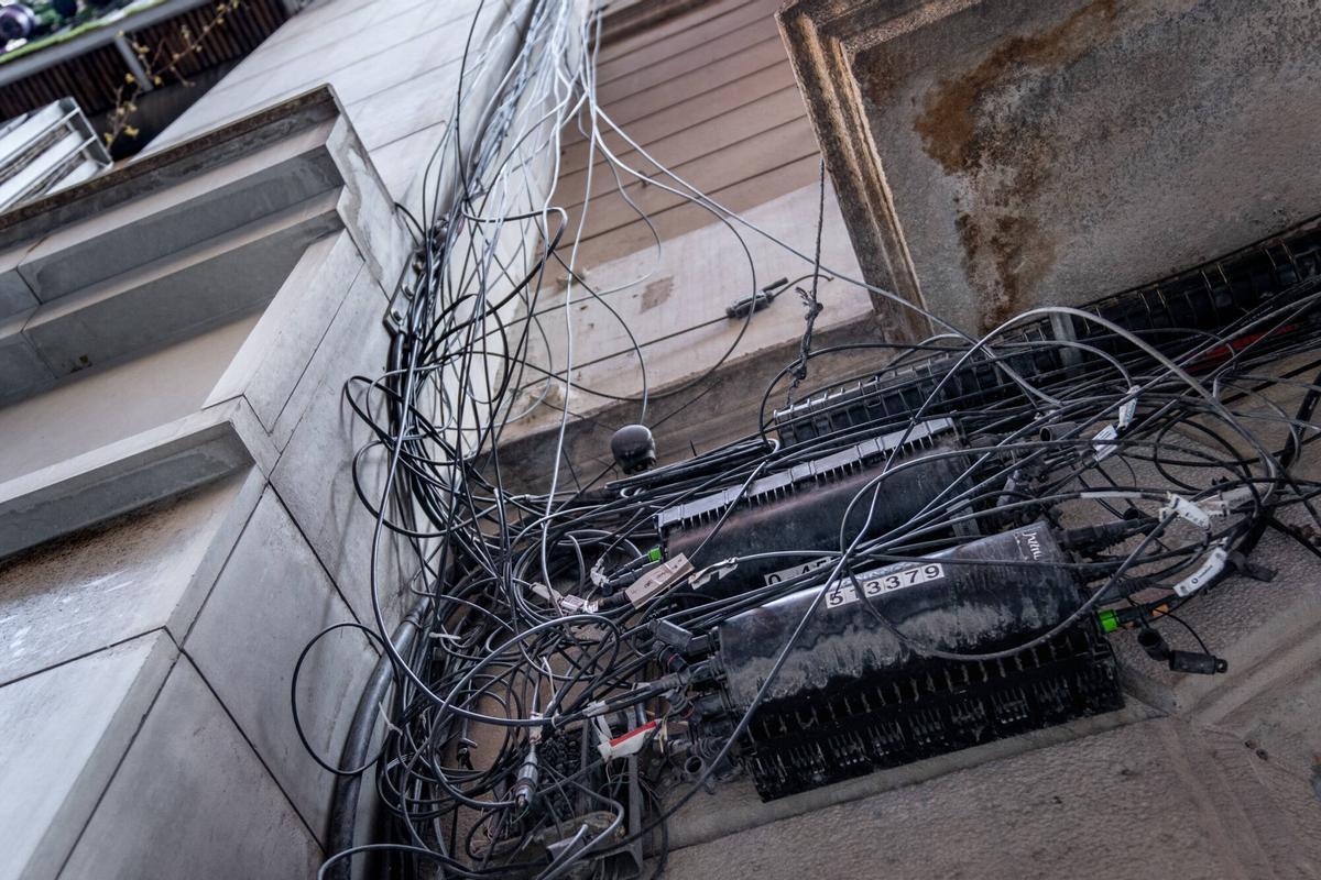 Imágenes de cableado eléctrico enmarañado en fachadas, bajantes y otros elementos de edificios, visibles desde la calle
