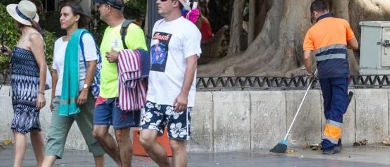 Un grupo de turistas pasa junto a un barrendero, en el entorno del Portal de Elche, en Alicante.