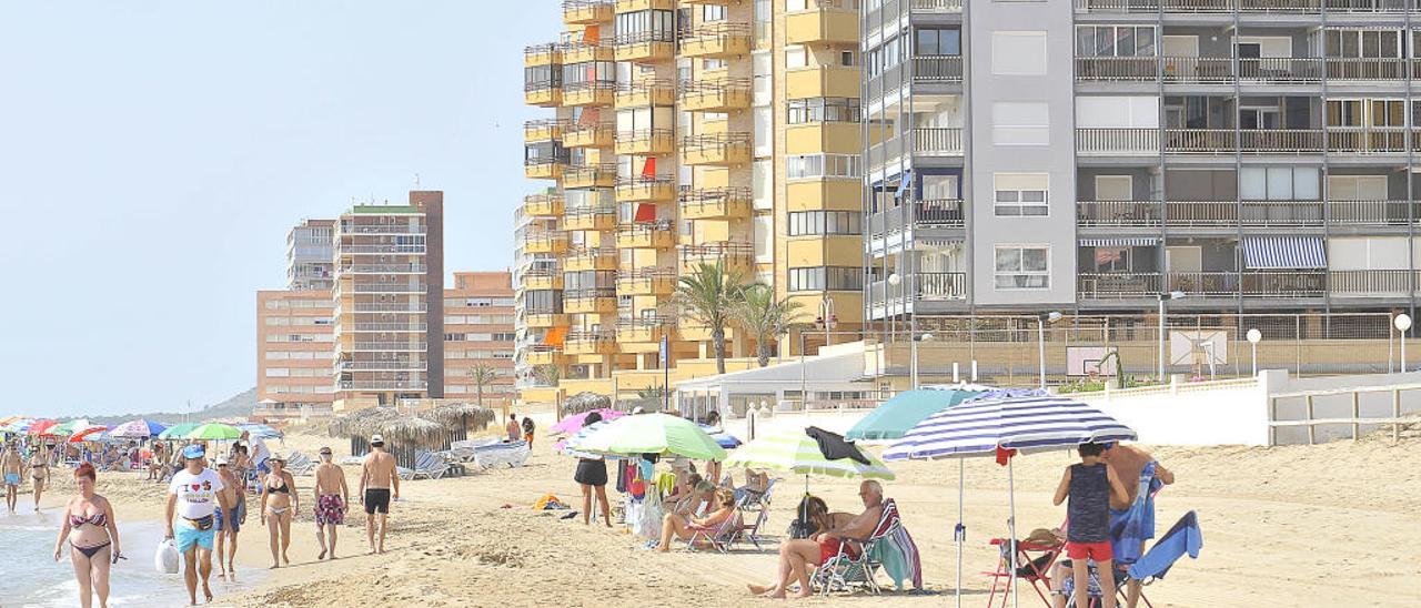 Veraneantes en la playa de Arenales del Sol, con edificios de apartamentos en la primera línea.