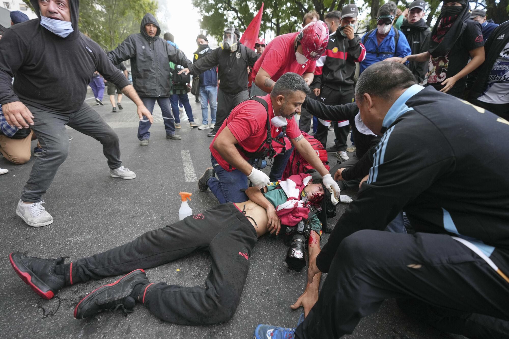 Medics tend to a photographer injured during clashes that broke out as soccer fans joined retirees demanding higher pensions and opposing austerity measures implemented by Javier Milei's government in Buenos AIres, Argentina, Wednesday, March 12, 2025. (AP Photo/Rodrigo Abd). EDITORIAL USE ONLY/ONLY ITALY AND SPAIN
