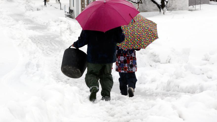 Un hombre camina con su nieto por la calle de un municipio valenciano totalmente nevado.