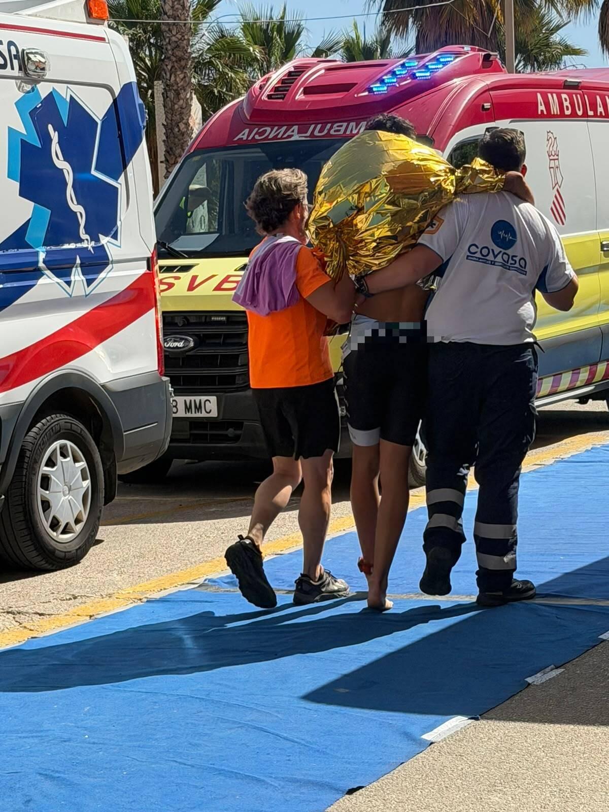 Un triatleta es llevado por dos personas hacia una ambulancia para recibir asistencia en el Triatlón de Tavernes de la Valldigna