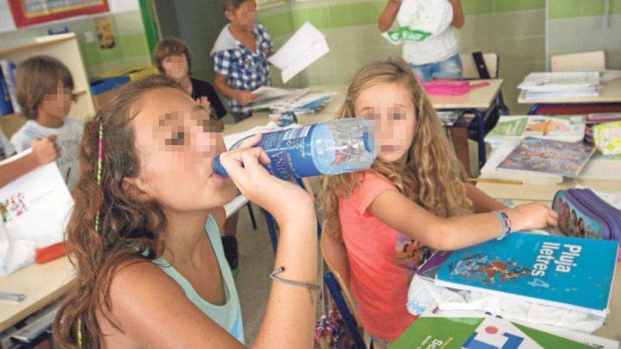 Una alumna de Primaria bebe agua por el calor en clase, con algunos libros en el pupitre.