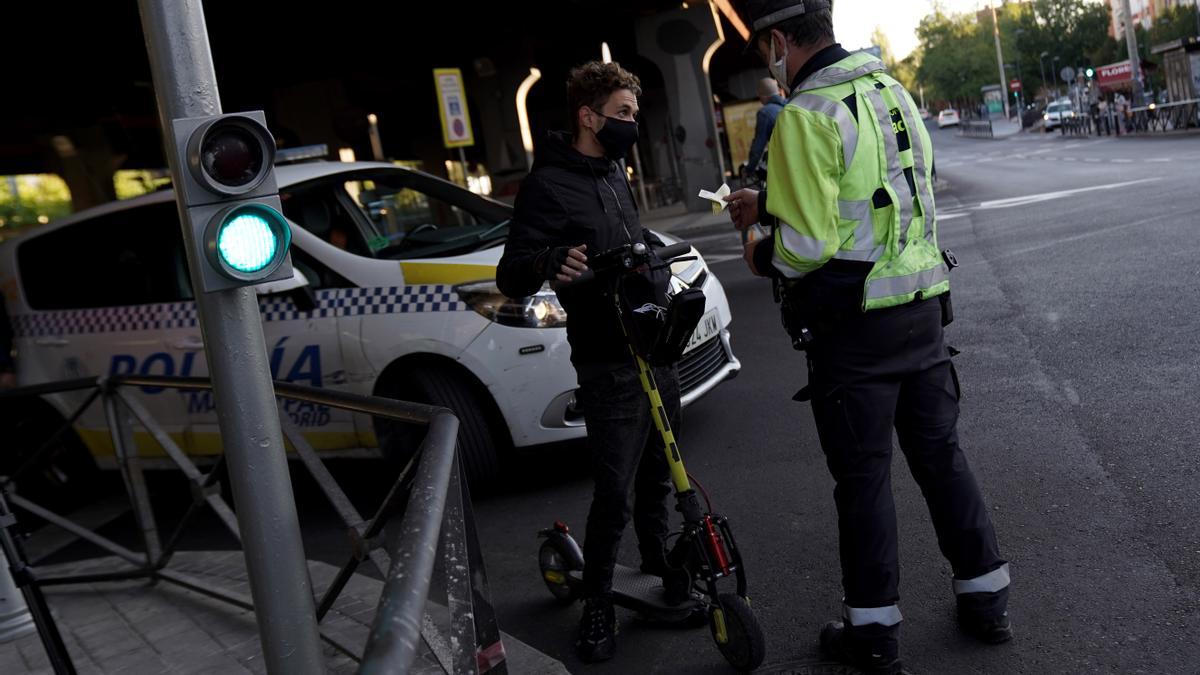 Un policía municipal multa a una persona en patinete eléctrico por acceder a una zona confinada en Madrid en 2020.