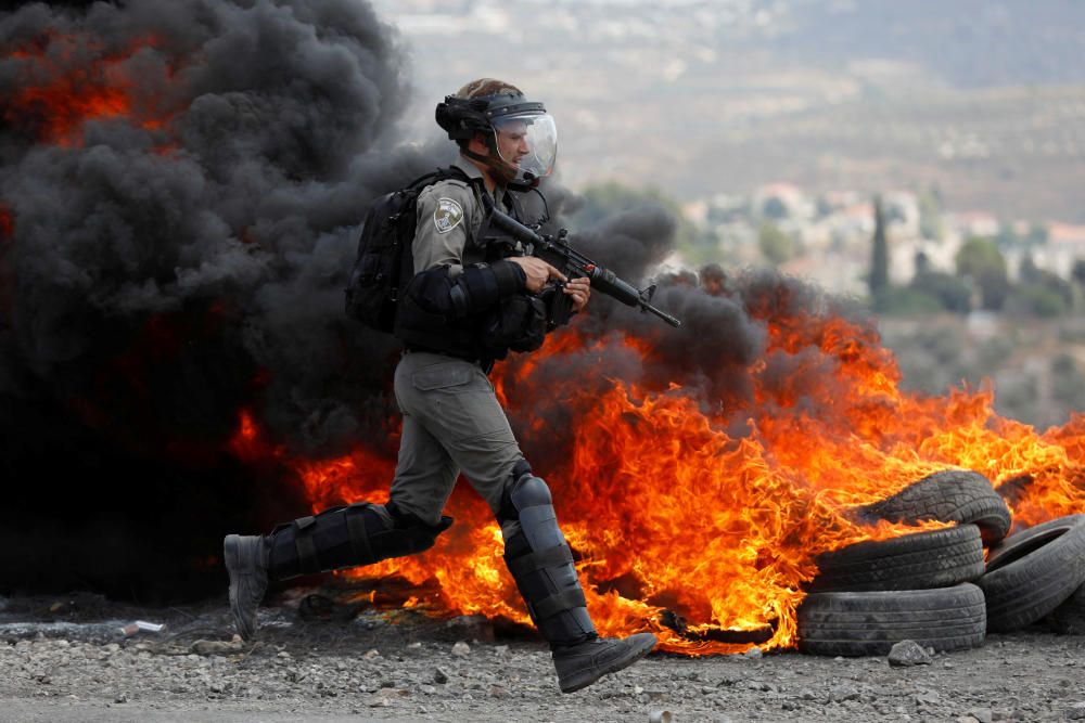 Un policía de la frontera israelí corre al lado de las llamas durante una protesta palestina contra el asentamiento judío en Qadomen, en la zona ocupada por Israel. REUTERS/Mohamad Torokman