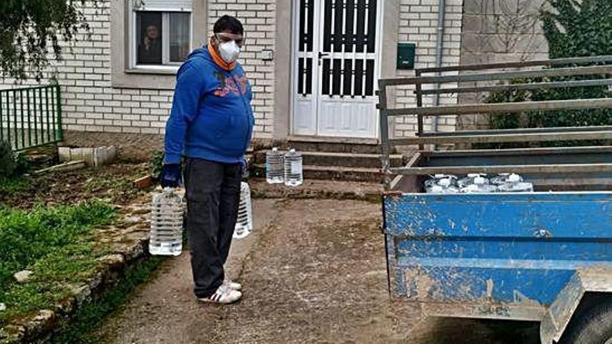 Un operario deja las garrafas de agua a la puerta de las casas provisto de mascarilla y guantes.