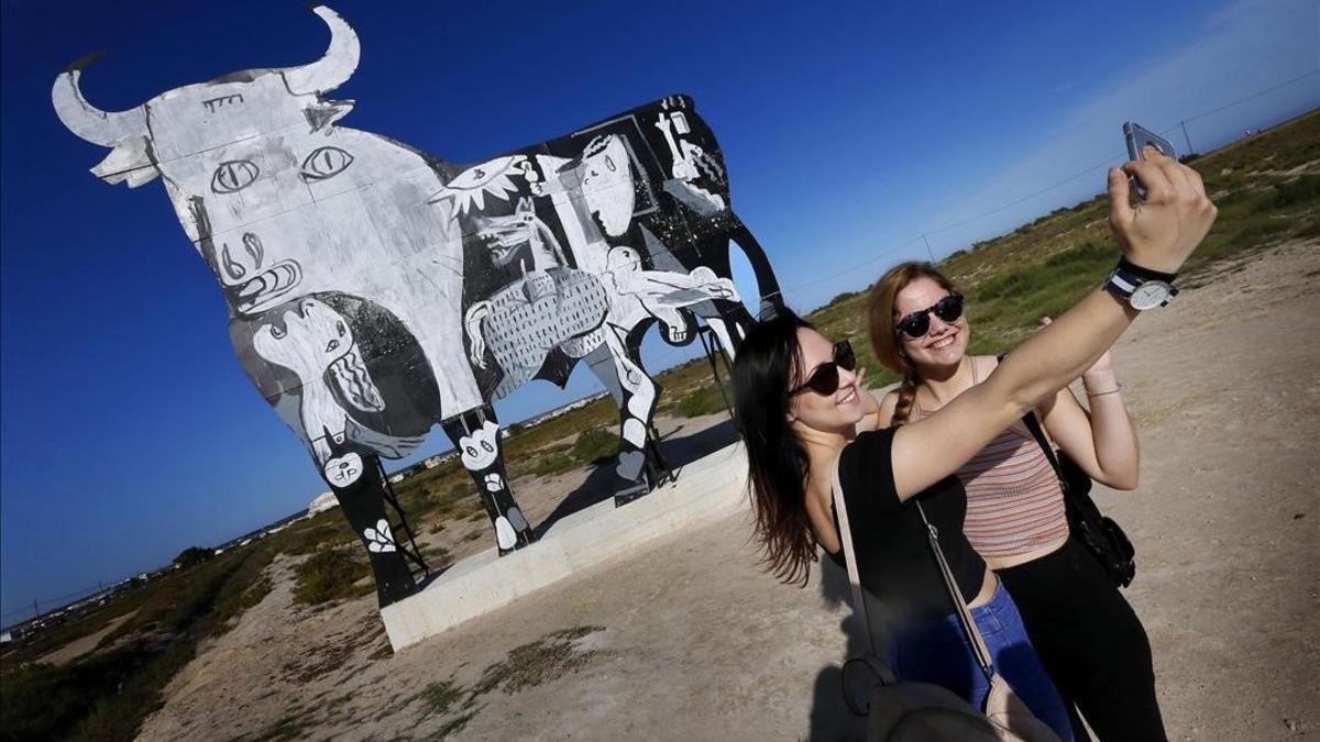 Turistas se acercan a fotografiarse y observar el toro de Osborne que ha aparecido pintado con el escenas del Guernica de Picasso en Santa Pola, Alicante.