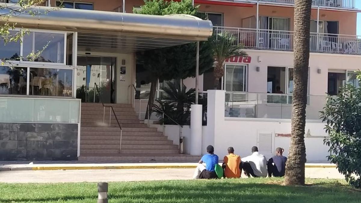 Varios jóvenes migrantes sentados frente a uno de los hoteles de Gandia donde se alojan.