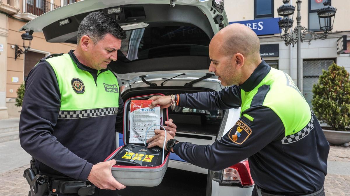Los dos agentes con el desfibrilador que llevan en el coche patrulla