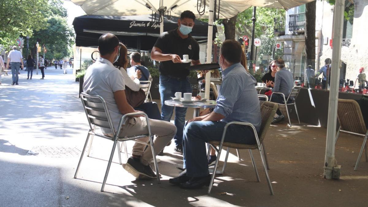 Un cambrer servint persones assegudes a la terrassa d&#039;un bar a la la Rambla de Catalunya en el primer dia de fase 1 a Barcelona