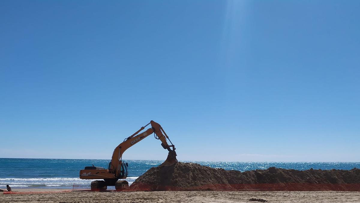 Imagen con un tractor junto a los montones de arena en la playa.